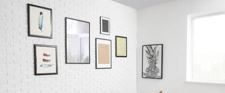 Framed artworks are arranged on a white brick wall inside a bright, minimalist interior space.