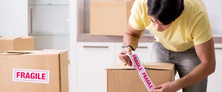 Worker sealing a fragile box with tape during careful packing by professional movers and packers in Dubai.