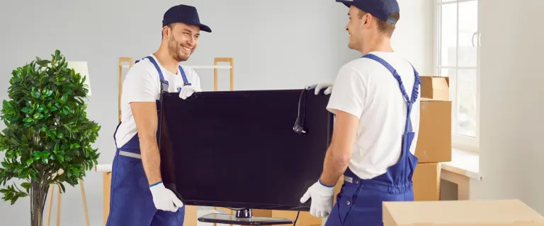 Technicians from UAE Movers are carrying a large monitor during an IT equipment moving service with safe handling procedures.