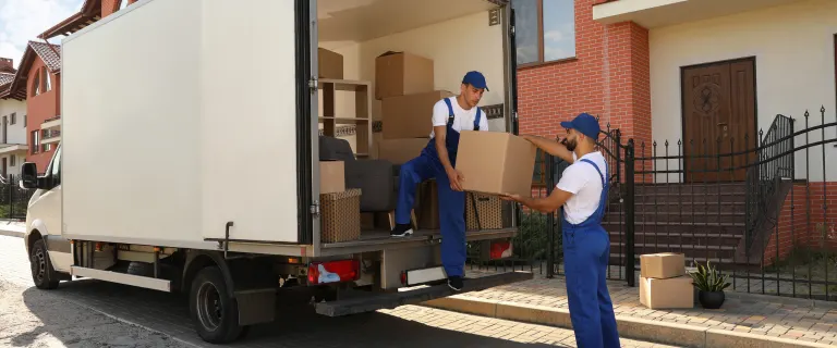 Movers unloading cardboard boxes from a relocation truck outside a residential property during a loading and unloading service.