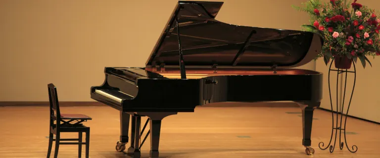 Elegant black grand piano positioned on a wooden stage floor with a chair and a floral arrangement beside it.