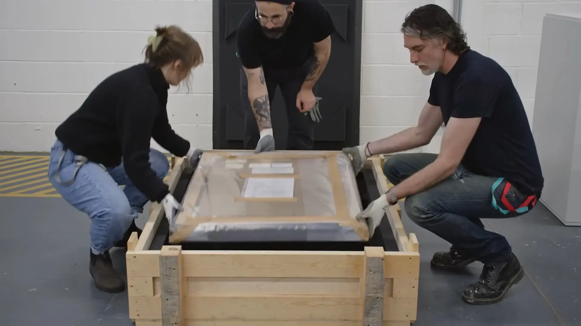 Fine art movers placing framed artwork into a custom wooden crate for secure transportation and international shipping.
